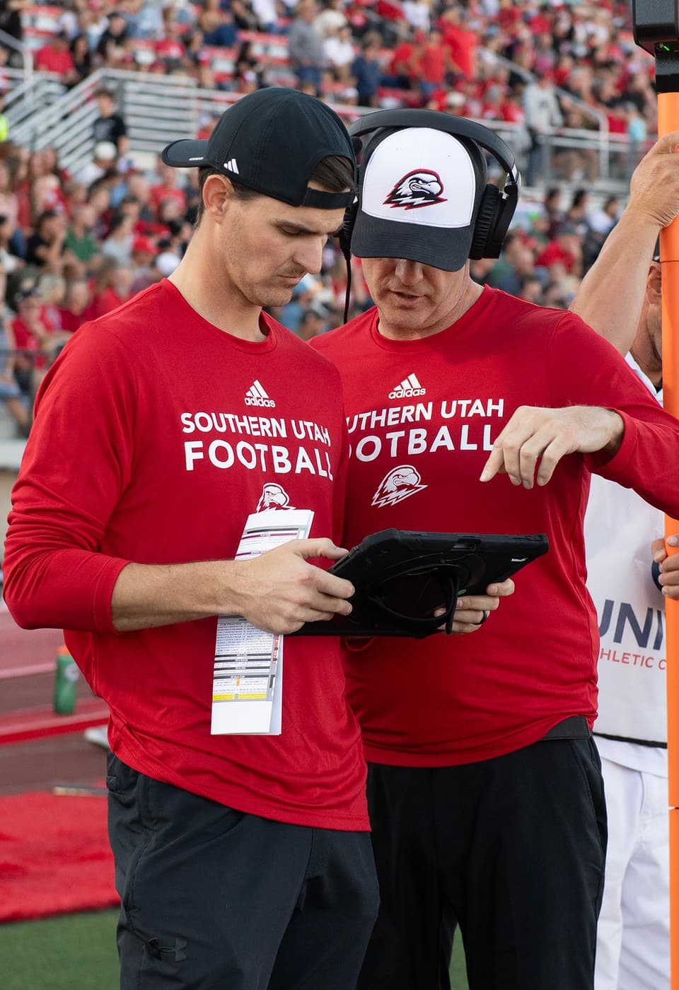 Two coaches reviewing notes on a tablet during a game